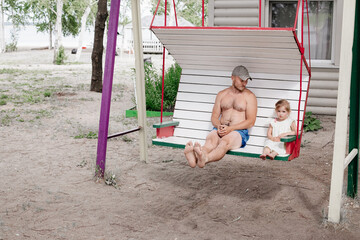 Father and daughter spend time in the backyard of the house. Family on a swing.