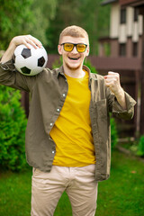 Excited young man holding soccer ball smiling and screaming, Happy male football fan support sport team, celebrating victory. People emotions, sports, entertainment concept, successful bet on sports