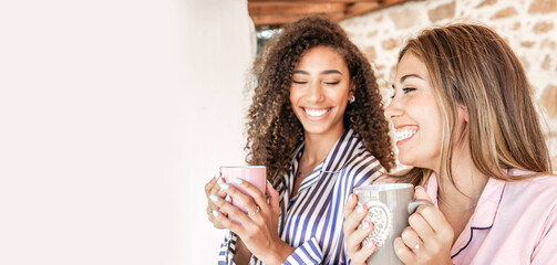 Multi-ethnic best friends women in pajama smiling holding a cup of tea with white copy space to the left - Concept: stay at home and enjoy your life
