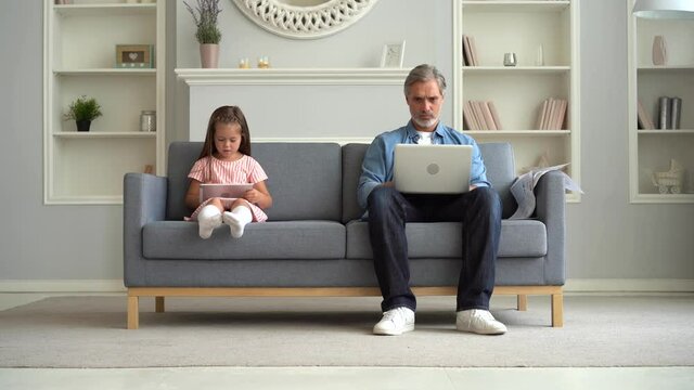 Father working at home with computer laptop and daughter playing on tablet in the living room