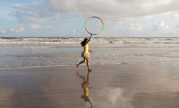 Teenage Girl Playing Holding Hula Hoop And Running In Sea Beach