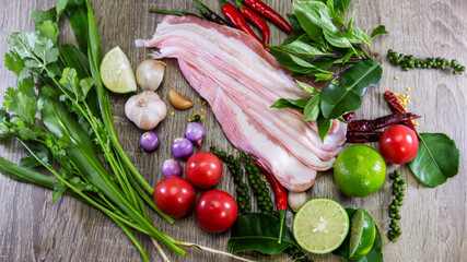 Pork belly cut into plates and placed on a wooden plate And spicy tom yum seasoning, chili, lime, coriander, garlic, onion, tomato, delicious cooking ideas