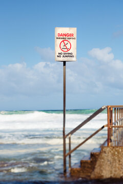 Danger sign beside rocky steps leading to a beach pool
