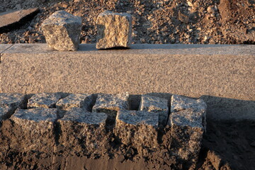 Granite cobblestones partially embedded in the ground at a construction site during sunset. Ideal for themes of roadwork, urban infrastructure, textures, and traditional paving
