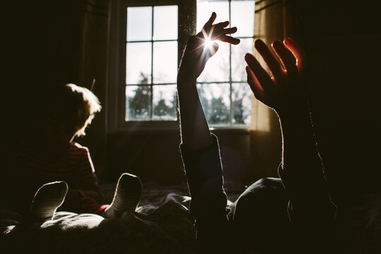 The sun in his hands. Children play on a bed in morning sun rays.