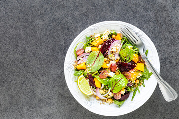 Fresh vegetable salad with beetroot, arugula, red onion, sorrel, chickpeas, pumpkin and grapes in a white plate on a black background. Top view