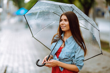 Cheerful woman holding umbrella while strolling outside. Beautiful woman with umbrella on a rainy...