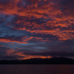 Bright and orange sunset at golden hour reflecting on calm Pacific Ocean water and over one 
dark Whitsundays island coast, Queensland, Australia