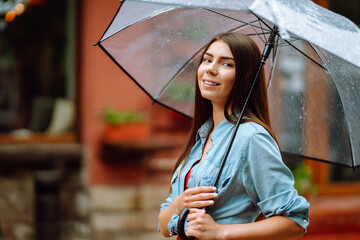 Cheerful woman holding umbrella while strolling outside. Beautiful woman with umbrella on a rainy day on the street. Autumn concept.