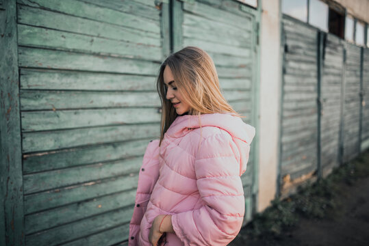 Young gorgeous blonde girl dressed fashion pink jacket and blue jeans. Old azure cerulean fence on the background. Picture ideal for illustrating women's magazines.