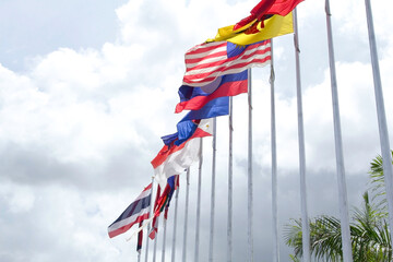 Many of the flags of ASEAN in the colorful colors blown by the force of the wind fluttering on a pole in front of a hotel in Thailand on a background with clouds and blue skies.