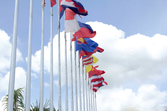Many of the flags of ASEAN in the colorful colors blown by the force of the wind fluttering on a pole in front of a hotel in Thailand on a background with clouds and blue skies.