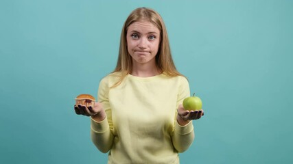 Young woman choosing between apple and cupcake, the girl is confused in her choice, isolated on a turquoise background. - Powered by Adobe