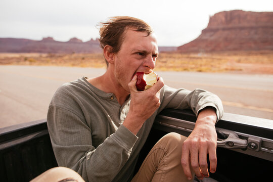 A young traveler bites into an apple while riding in the back of a truck