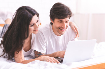 Fototapeta premium Young couple browsing on laptop in bed