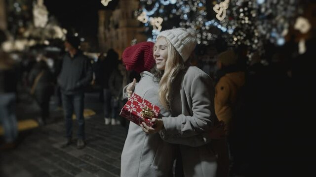 Two friends presenting gifts to each other at xmas night at old town square. Friendship, christmas, new year, holiday concept. Filmed on RED camera, 10 bit clolor