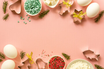Flat lay of christmas cookie cutters and baking ingredients on a pink background. Space for text