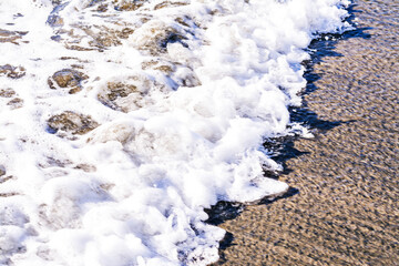 Close up of bubbling sea wave rolling over sand beach