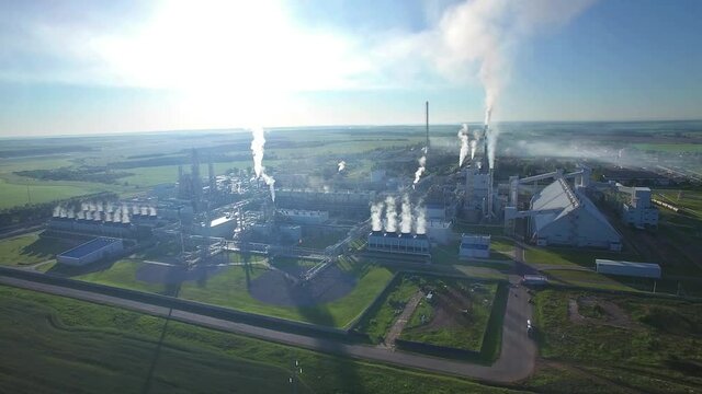 Chemical Plant produces gasoline and mineral fertilisers. Aerial orbit circle flying morning sunshine summer fields and grass around. Smoke smog and environmental pollution.