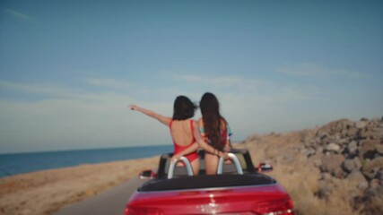 Two female friends enjoying traveling in the car In Greece on the island of Crete. Girls blow a kiss and ride a cabriolet along the sea. The concept of freedom, friendship, free love. Filmed 4K,10bit. - Powered by Adobe