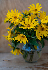 A bouquet of yellow Jerusalem artichoke flowers in a glass vase on a wooden background. Postcard with place for text. A simple wild flower that looks like a chamomile. Copy space.