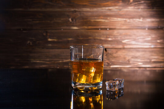 Glasss of whiskey with ice cubes on dark wooden background