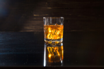 Glasss of whiskey with ice cubes on dark wooden background