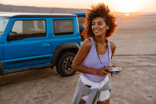 Image of african american girl holding retro camera in desert