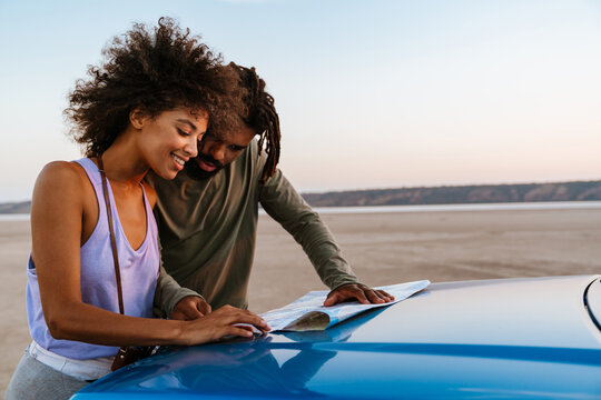 Image of joyful african american couple examining map while travelling on desert