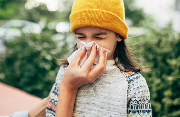 Outdoor portrait of a little girl sneezing the nose into the tissue.