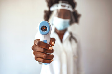 Woman doctor in safety face mask and white coat holding infrared thermometer, standing isolated on...
