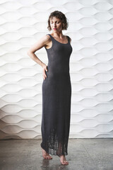 A woman in a grey knitted dress stands against a white wall