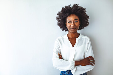 Portrait of beautiful cheerful girl smiling and looking at camera. Happy african woman in casual standing on white background. Stylish woman with crossed arms and curly hair isolated with copy space.