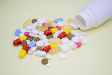 Multicolored pills fall out of a white bottle on yellow background