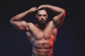 Muscular guy with black beard and mustache staying and combing his hairs in dark studio background.