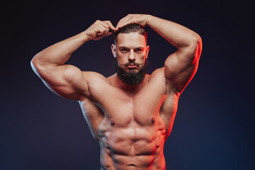 Brutal and muscular bodybuilder with dark beard posing with and combing his hairs with hairbrush in...