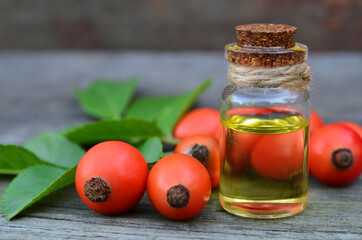 Rosehip essential oil in a glass bottle with rose hips berries on old wooden table for skin care or spa.Selective focus.