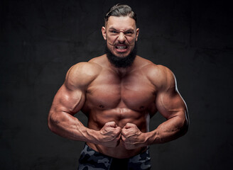 Fototapeta premium Self confident and aggressive military bodybuilder with naked torso and with black beard posing in gray background.