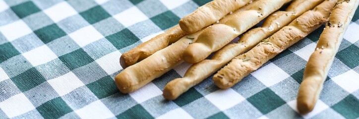 Breadsticks or Italian grissini snack on green gingham tablecloth. Food, gastronomy, cuisine, culture concept. Copy space. Banner