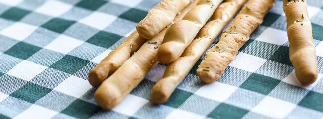 Breadsticks or Italian grissini snack on green gingham tablecloth. Food, gastronomy, cuisine, culture concept. Copy space. Banner