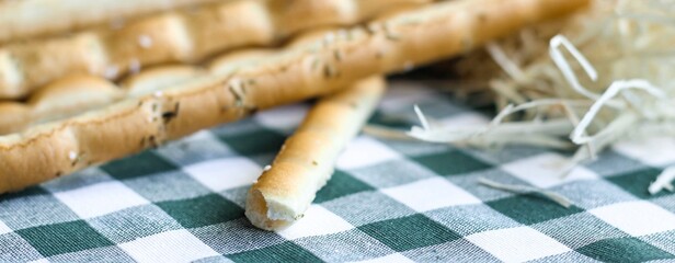 Breadsticks or Italian grissini snack on green gingham tablecloth. Food, gastronomy, cuisine, culture concept. Copy space. Banner