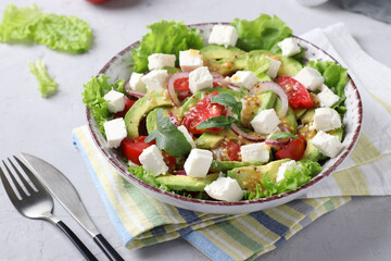 Healthy salad with avocado, tomatoes, feta and red onion on grey background, closeup
