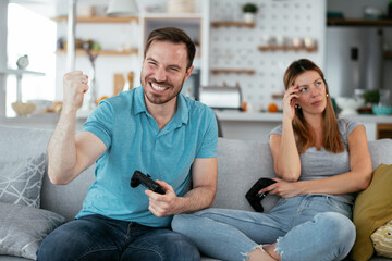 Obraz premium Husband and wife playing video game with joysticks in living room. Loving couple are playing video games at home..
