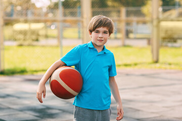 Portrait of a smiling boy in a sports uniform with a basketball in his hands. A boy holds a ball in his hands after playing basketball.