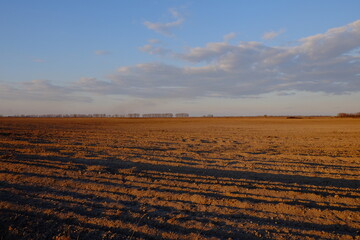 Cloudy evening sky over an empty agricultural field. Bright sunset landscape.