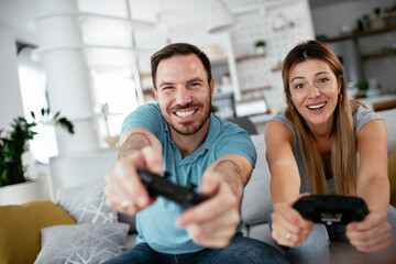Obraz premium Husband and wife playing video game with joysticks in living room. Loving couple are playing video games at home..