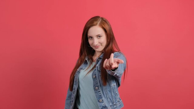 Come to me. Close up of a young woman that pointing at someone to come, isolated on red background.