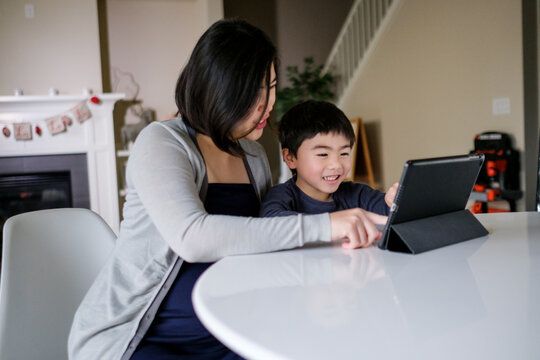 Pregnant Asian woman playing game on tablet PC with her son