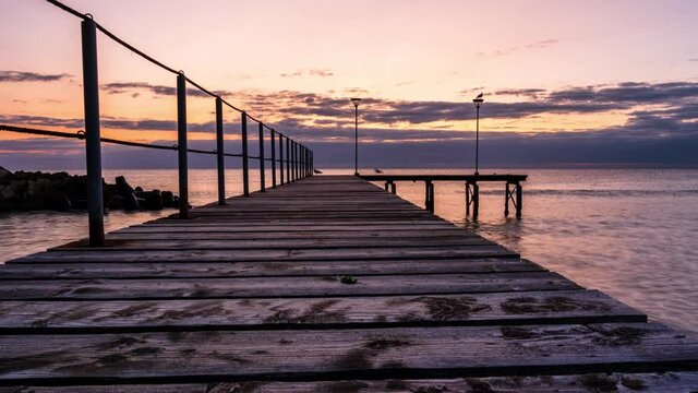 Timelapse with the rising sun and a wooden bridge at the sea coast