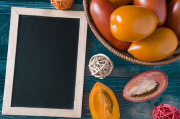 red and orange oval tomatoes and half a tomato on a wooden background dark placard for text